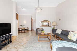 Ein modernes Wohnzimmer mit Flachbildfernseher, einer Couch, einem Couchtisch und einem Essbereich mit Tisch und Stühlen.