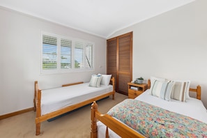 Ein Schlafzimmer mit zwei Einzelbetten, einem Holzschrank, einem Nachttisch mit Pflanze und einem Fenster mit Jalousien.