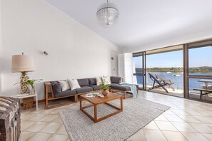 Ein modernes Wohnzimmer mit Sofa, Couchtisch und Meerblick durch große Fenster.