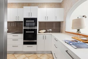A modern kitchen with white cabinetry, a double oven, and a wooden countertop. - Commodore 8 - Top Floor Views (Noosa Heads)