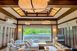 A spacious living area with a large sofa, a television, and a ceiling light fixture. - Krajokkaew Inyeon Khao Yai (Pak Chong)