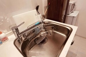 Un évier de cuisine en acier inoxydable, avec un égouttoir à vaisselle, une planche à découper et une bouteille de liquide vaisselle.