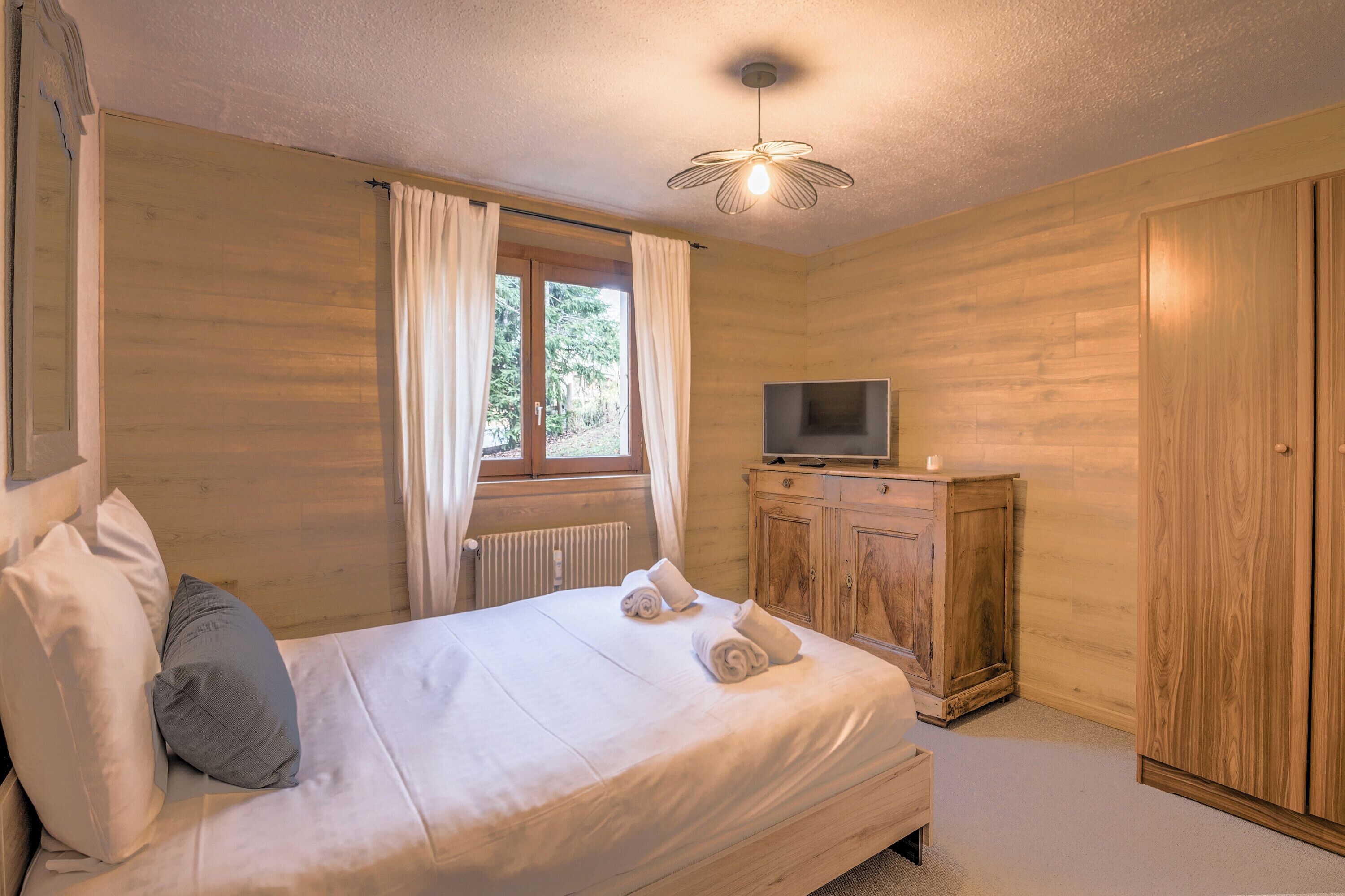 Ein Schlafzimmer mit einem Bett, einem Fernseher auf einem Holzschrank und einem Fenster mit Vorhängen.
