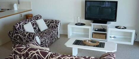 A living room with a sofa set, a coffee table, a TV, and a small shelf with items.