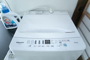 Una lavadora Hisense con panel de control, una botella de detergente Attack y una pared blanca.