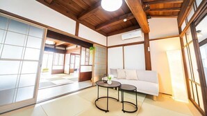 Una habitación al estilo japonés tradicional, con suelo de tatami, un sofá blanco, dos mesitas y un ventilador de techo.