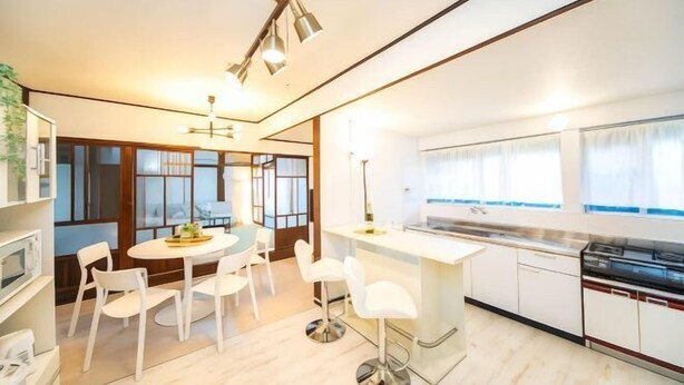Una cocina moderna con armarios blancos, una isla central con taburetes y una zona de comedor con una mesa redonda y sillas.