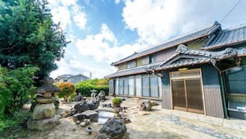 A traditional Japanese building with a tiled roof, a wooden entrance, and a garden with rocks and plants.