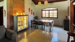 A spacious living area with a high ceiling, a dining table with chairs, a sofa, and a cabinet with glass doors. - House with pool and 4 suites in Bertioga (Bertioga)