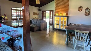 A spacious living area with a high ceiling, a dining area with a wooden table and chairs, and a kitchen with a brick wall and hanging light fixtures. - House with pool and 4 suites in Bertioga (Bertioga)