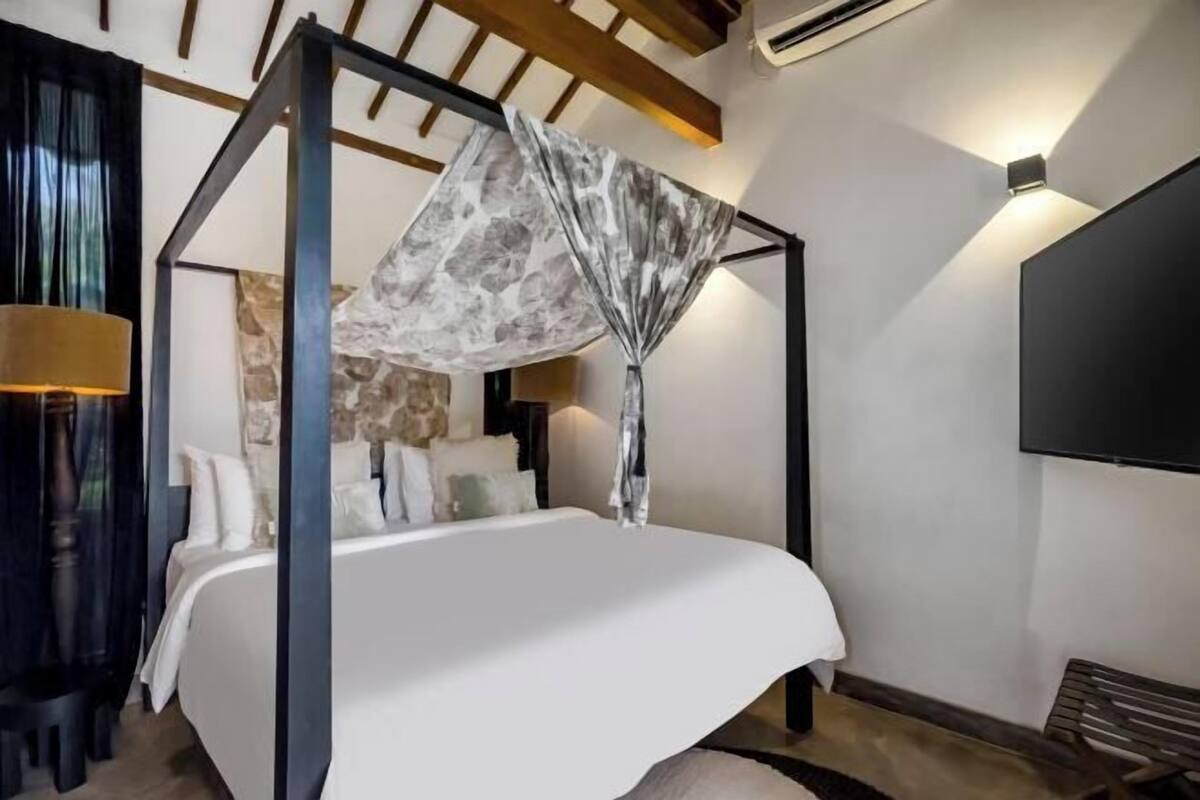 A four-poster bed with a canopy, a flat-screen TV, and a stone accent wall.