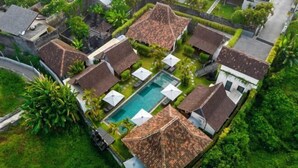 An aerial view of a resort with multiple bungalow-style buildings, a central swimming pool, and lush greenery surrounding the property. - Bloom Resort Bali by BaliSuperHost (Bali)