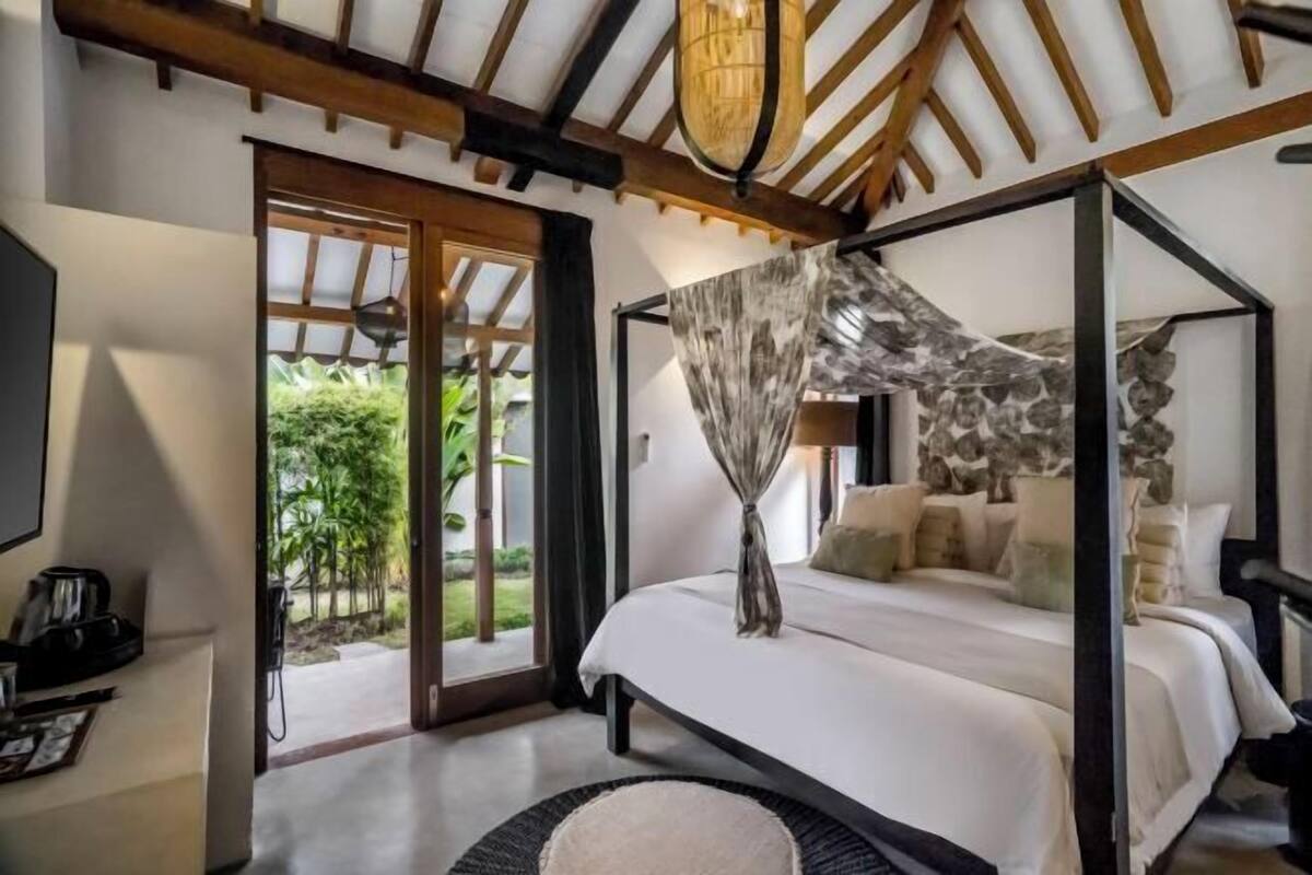 A bedroom with a four-poster bed, a large window, and a view of greenery outside.