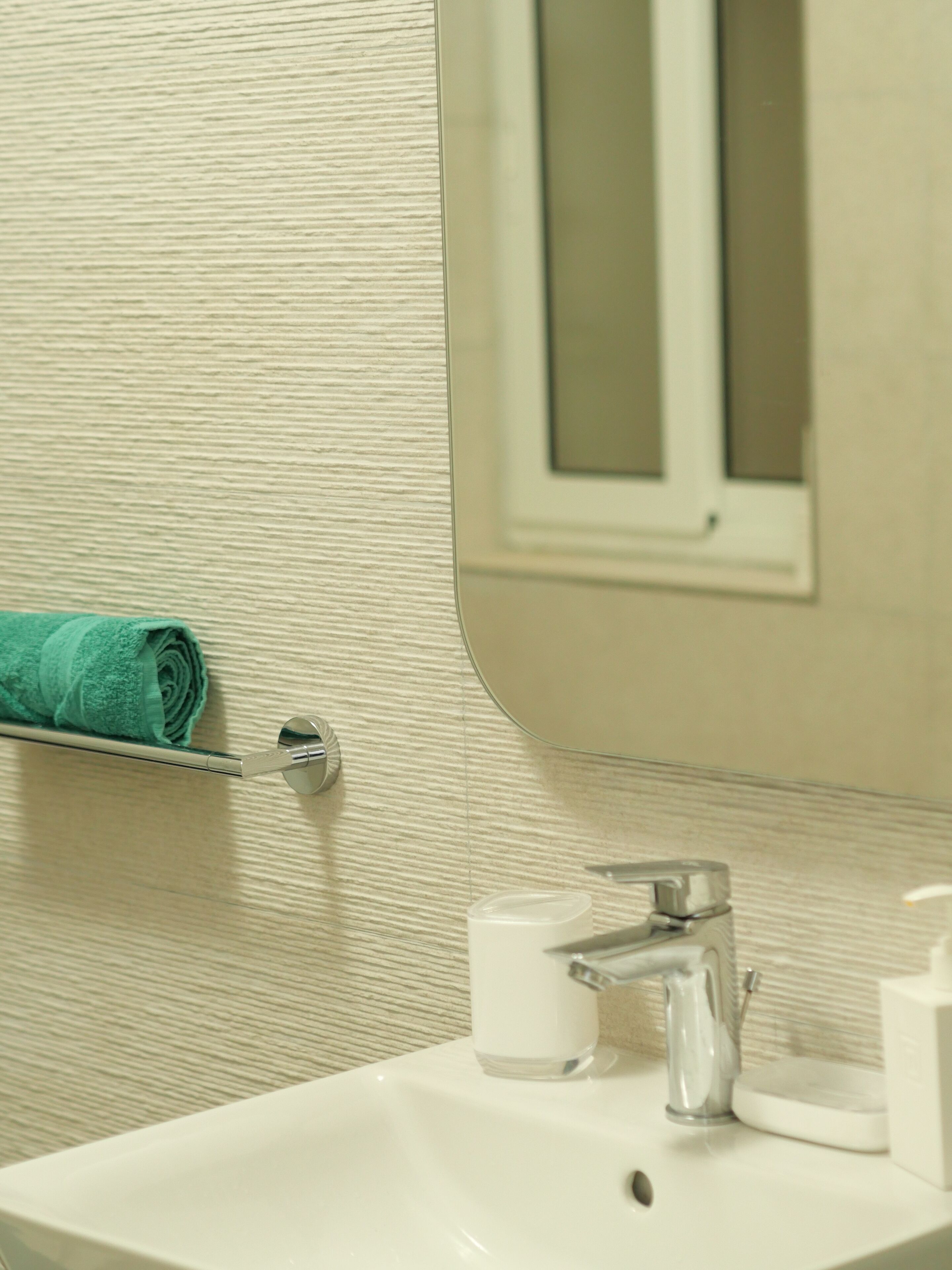 A bathroom with a white sink, a mirror, and a towel rack with a rolled towel.