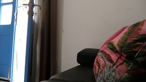 Een kamer met een blauwe deur, een zwarte bank en een geborduurde plaid.