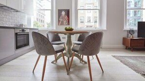 A modern kitchen with a dining table and chairs, large windows, and a view of buildings outside. - 3VH Virginia House, 31 Bloomsbury Way by City Living London (London)