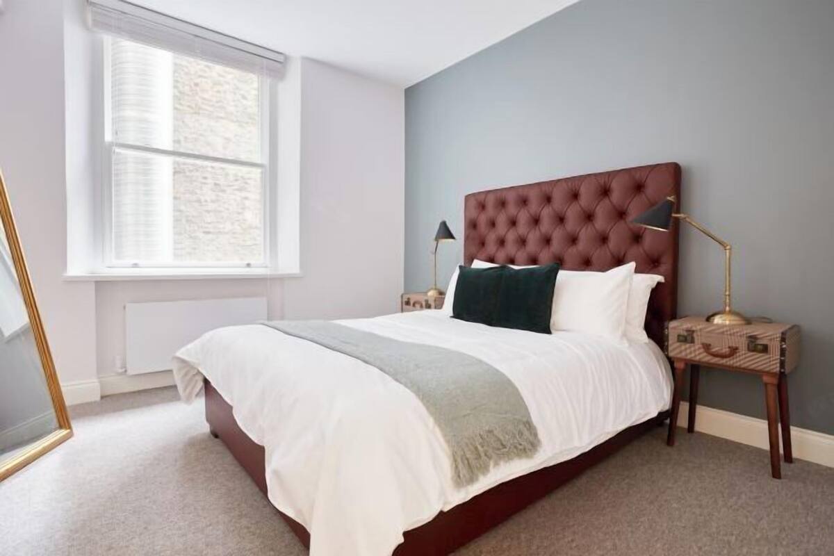 A bedroom with a large bed, a nightstand, a lamp, and a window.