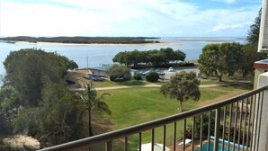 A balcony with a view of a swimming pool, a grassy area, and a body of water in the distance. - Sails Unit 25 (Sunshine Coast)