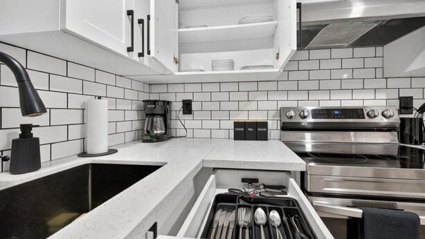 A modern kitchen with white cabinets, a black faucet, a coffee maker, and a stainless steel oven. - The Millertime Den (Brantford)