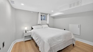A bedroom with a bed, bedside table, and a window with curtains. - The Millertime Den (Brantford)