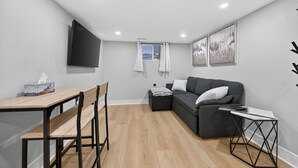 A modern living room with a wooden dining table, a grey sofa, and a small side table. - The Millertime Den (Brantford)