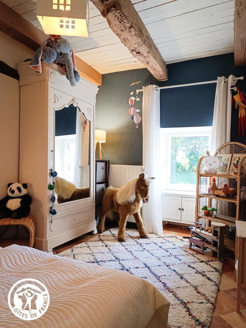 Ein Kinderzimmer mit Bett, Kommode, Spiegel, einem hängenden Elefanten, einem Plüschpanda, einer kleinen Pferdefigur und einem Bücherregal mit Spielzeug.