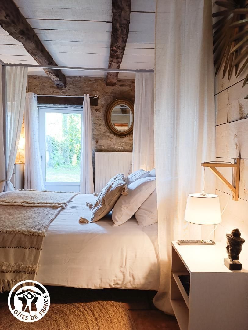 Un dormitorio con una cama, una mesita de noche, una lámpara y una ventana con cortinas.