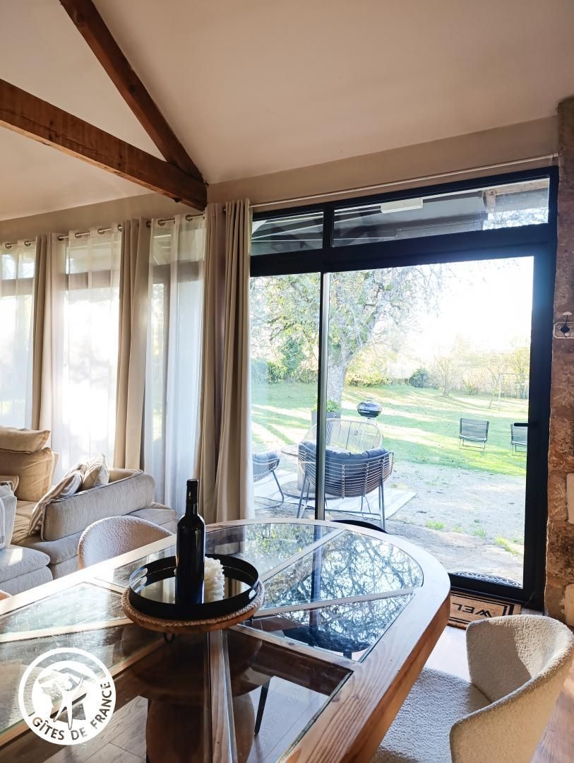 Ein modernes Wohnzimmer mit einem Glastisch, einer Couch und Blick auf eine Terrassenanlage mit Stühlen und einem Tisch.