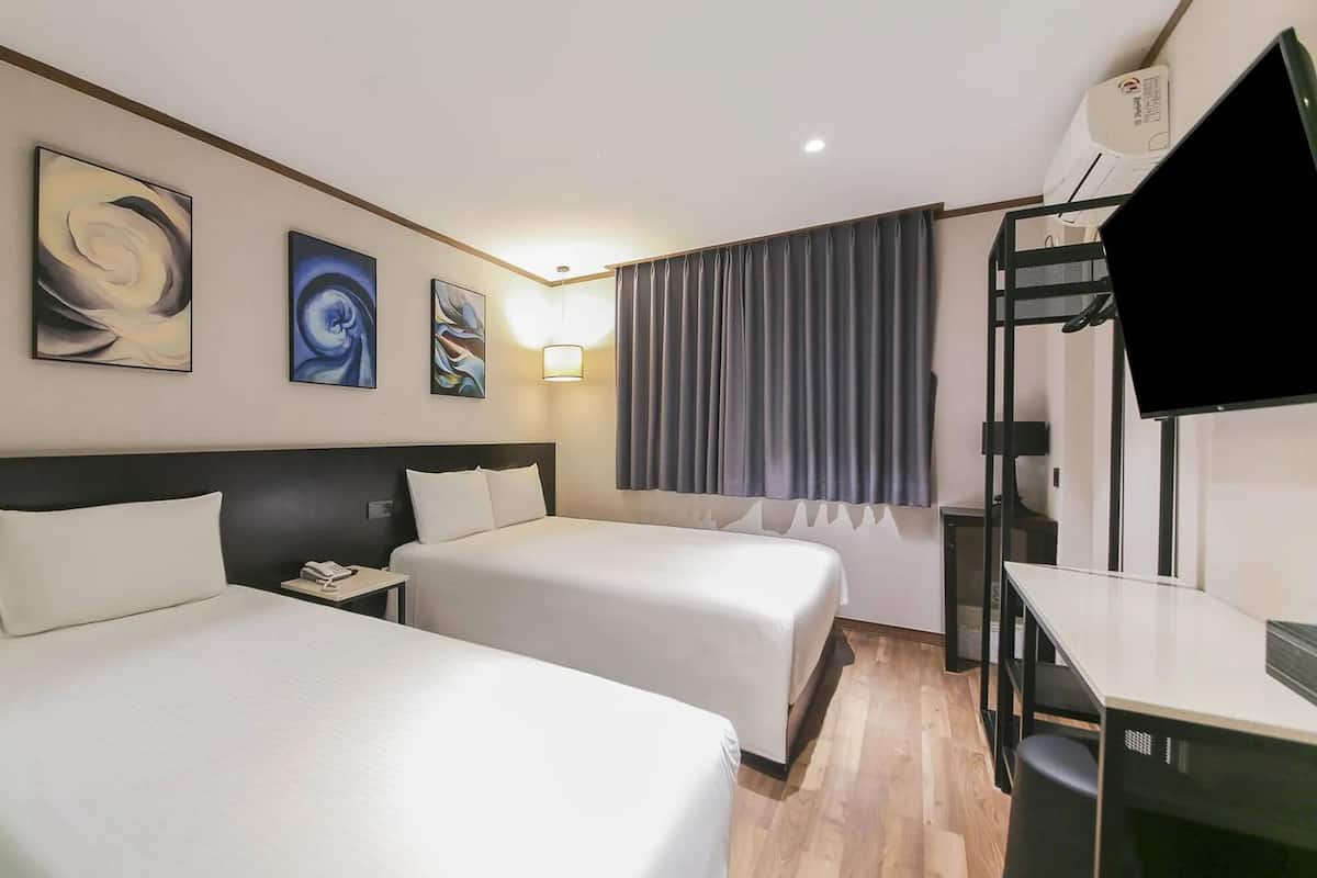 Habitación de hotel con dos camas, un escritorio, una silla, un televisor y una obra de arte en la pared.