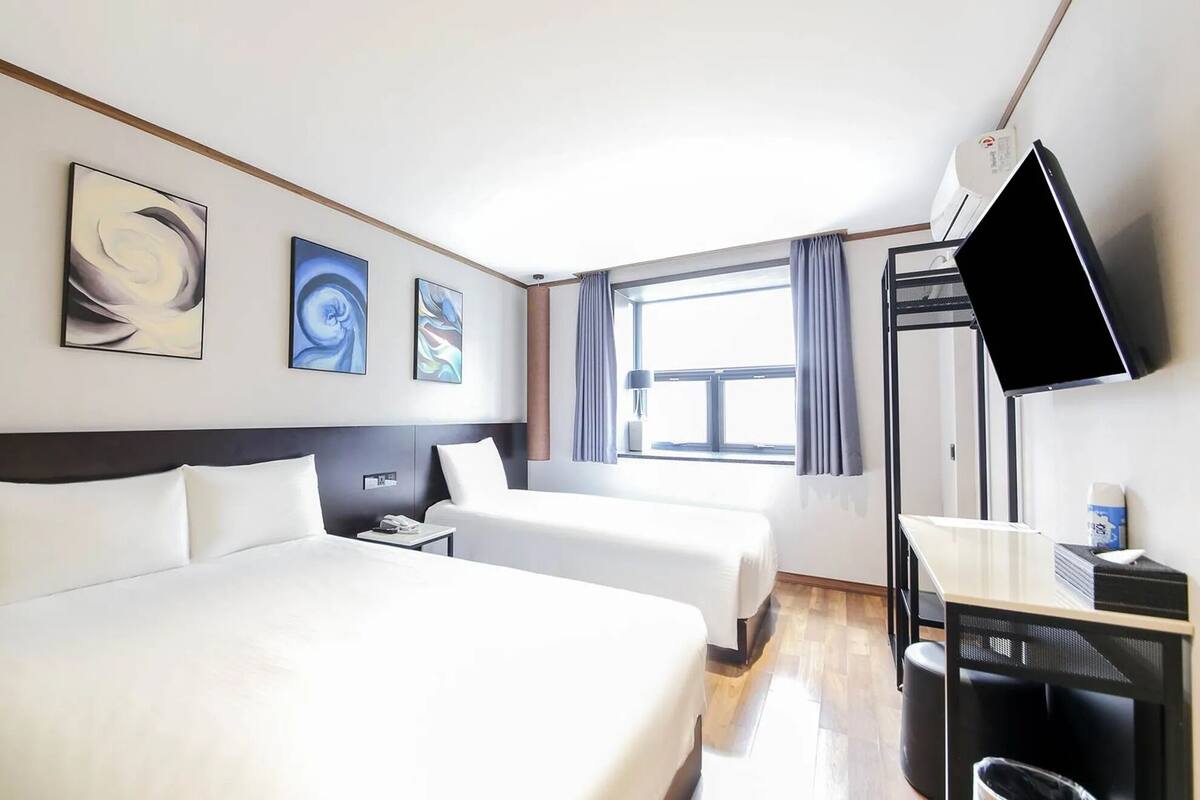 Habitación de hotel con dos camas, un escritorio, un televisor y obras de arte en la pared.