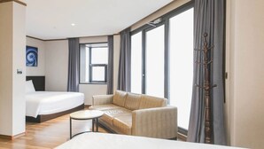 Una habitación de hotel con cama, sofá, una mesita y un ventanal con cortinas.