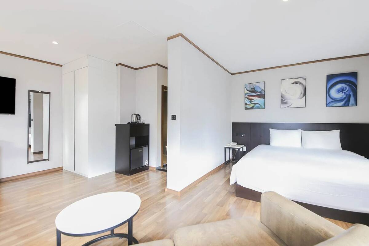 Habitación de hotel con una cama grande, un escritorio, una silla, un televisor y obras de arte en las paredes.