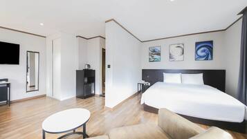 A hotel room with a large bed, a desk, a chair, a TV, and artwork on the walls.