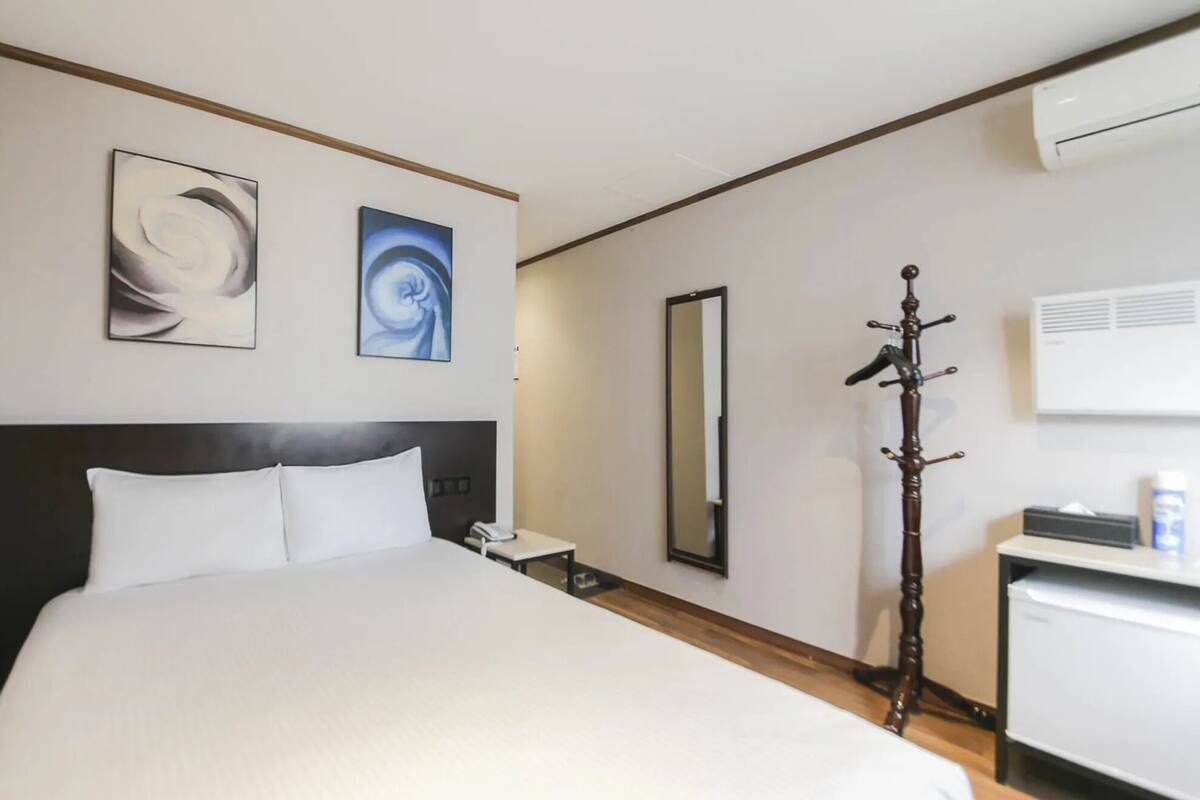 Habitación de hotel con una cama grande, una mesita de noche con teléfono, un espejo y un perchero.