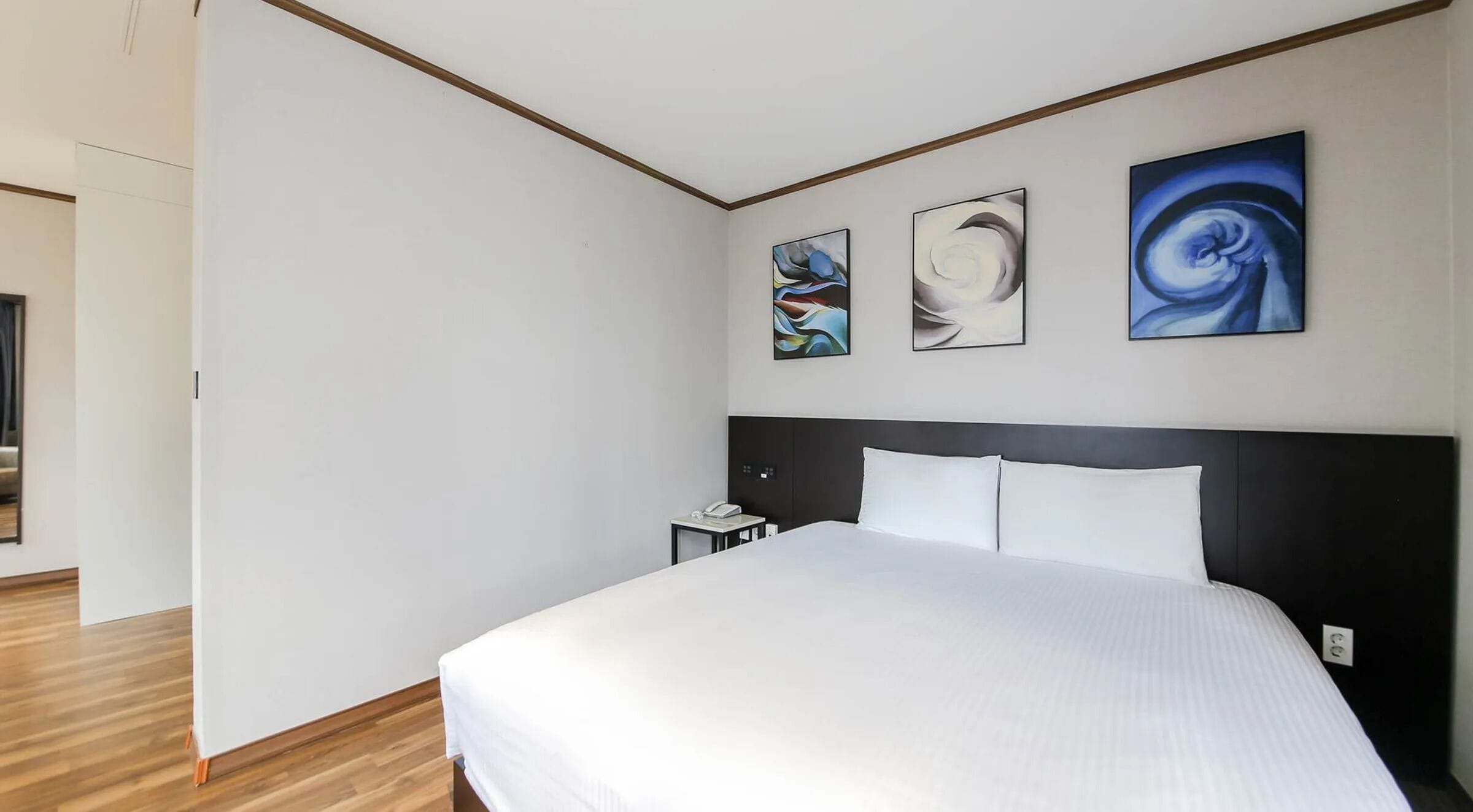 A hotel room with a large bed, a nightstand, and three abstract paintings on the wall.