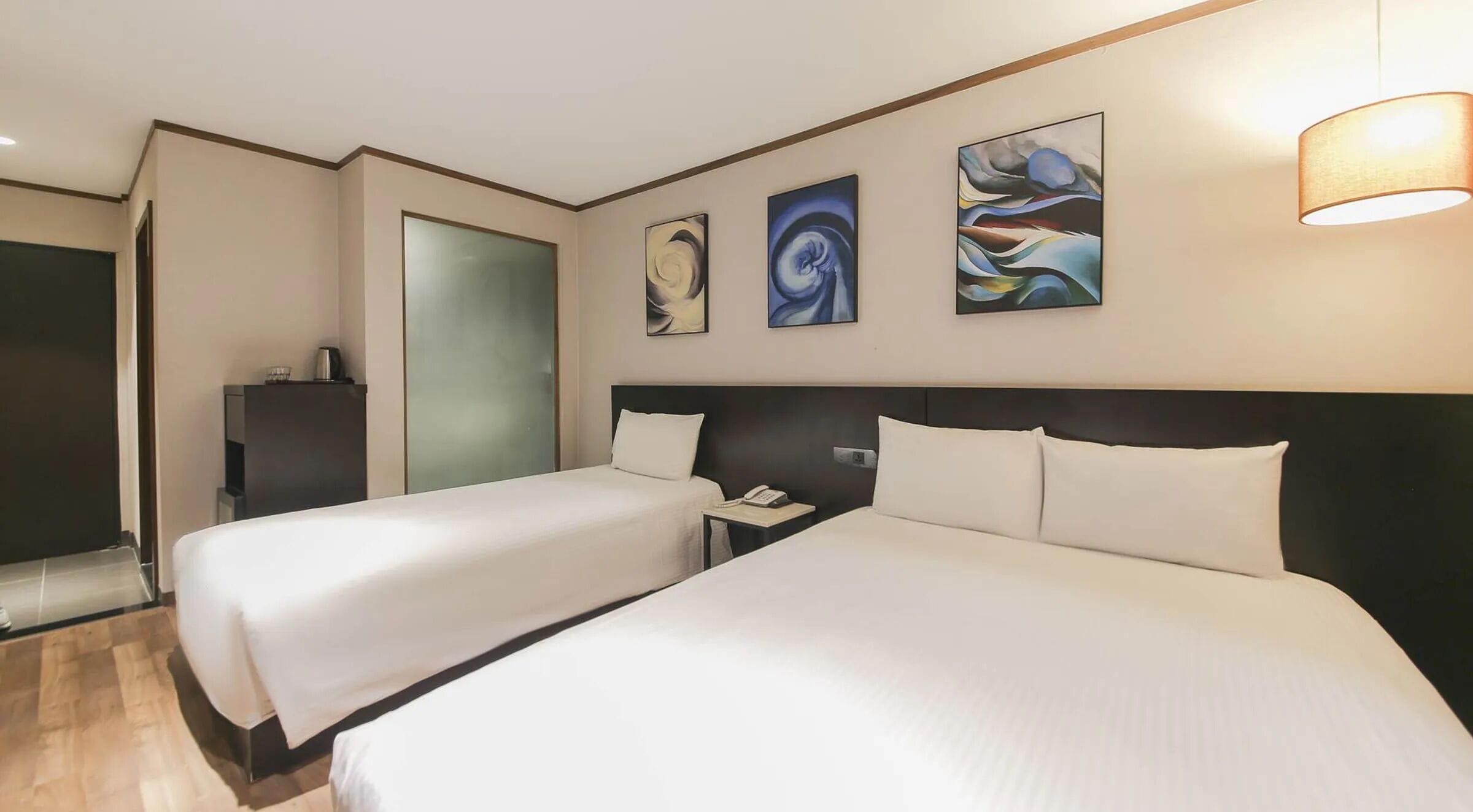 A hotel room with two beds, a nightstand, a phone, and abstract wall art.