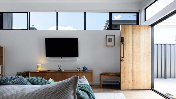 A modern bedroom with a large window, a flat-screen TV, a wooden door, and a cozy bed with pillows. - South Launceston – Easy & Comfortable (Launceston City)