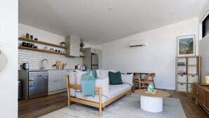 A modern kitchen with white cabinets, a dishwasher, and a refrigerator. There is a wooden dining table with chairs and a white rug on the floor. - South Launceston – Easy & Comfortable (Launceston City)