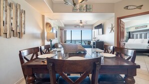 A dining area with a large wooden table, chairs, and a view of the ocean through large windows. - Luxury Beachfront Stay at Las Palomas A702 Phase 1 – Stunning 2BR Escape on Sandy Beach (Puerto Peñasco)
