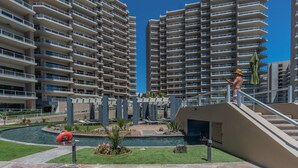 A high-rise residential building with multiple balconies, a swimming pool, and a landscaped garden area. - Luxury Beachfront Stay at Las Palomas A702 Phase 1 – Stunning 2BR Escape on Sandy Beach (Puerto Peñasco)