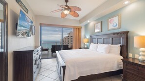 Een hotelkamer met een bed, een dressoir, een plafondventilator, uitzicht op de oceaan en een balkon.
