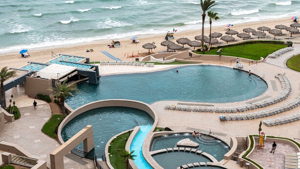 Een resort met een groot zwembad, een apart bubbelbadgedeelte en een strand met parasols.