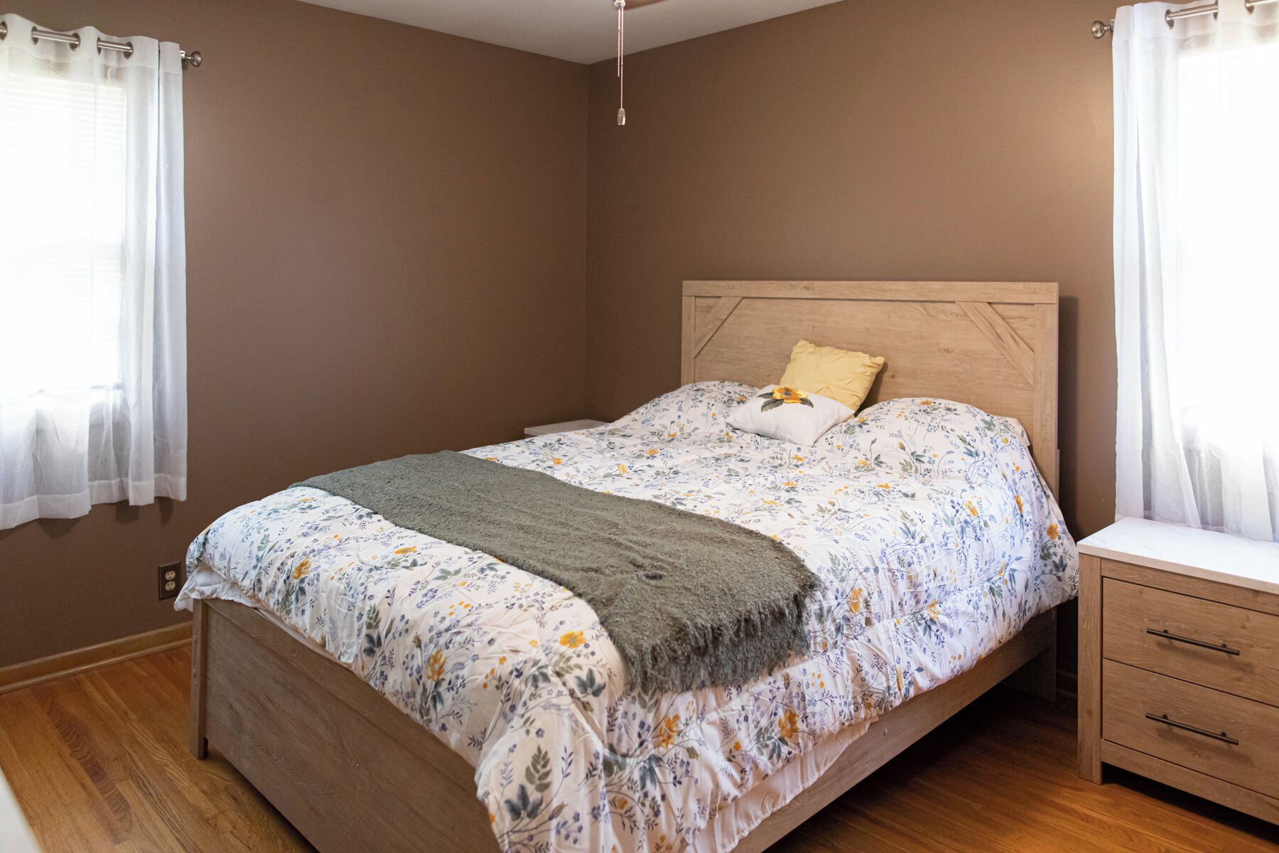 Une chambre à coucher avec un lit en bois, une literie à motifs floraux, une table de chevet et des rideaux.