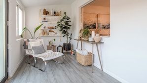 Ein gemütlicher Winkel mit einem gepolsterten Sessel, einem kleinen Tisch, einem Bücherregal und einem großen Fenster.