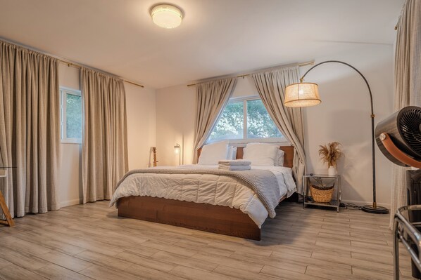 A bedroom with a wooden floor, a bed with a white duvet, a standing lamp, and a window with curtains. - MIA Villa — Spacious Miami Getaway with Outdoor Kitchen & Central Location (Miami)