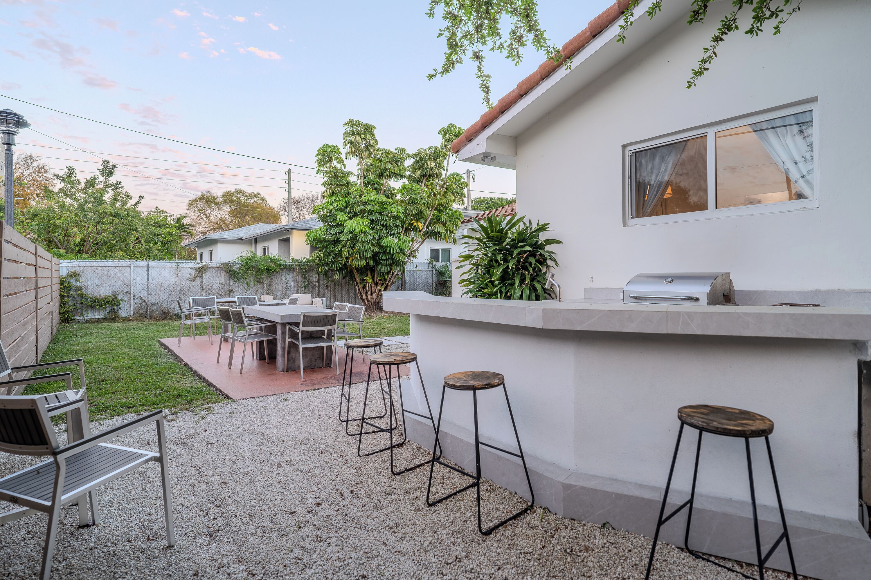 Un espace patio comprenant un coin barbecue, des sièges d’extérieur et un bâtiment blanc doté d’une fenêtre.