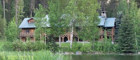 A rustic lodge with a large deck and a pond in front.