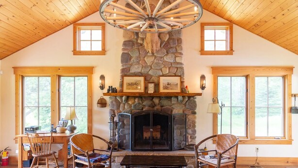 A cozy room with a stone fireplace, wooden ceiling beams, and a rustic chandelier.