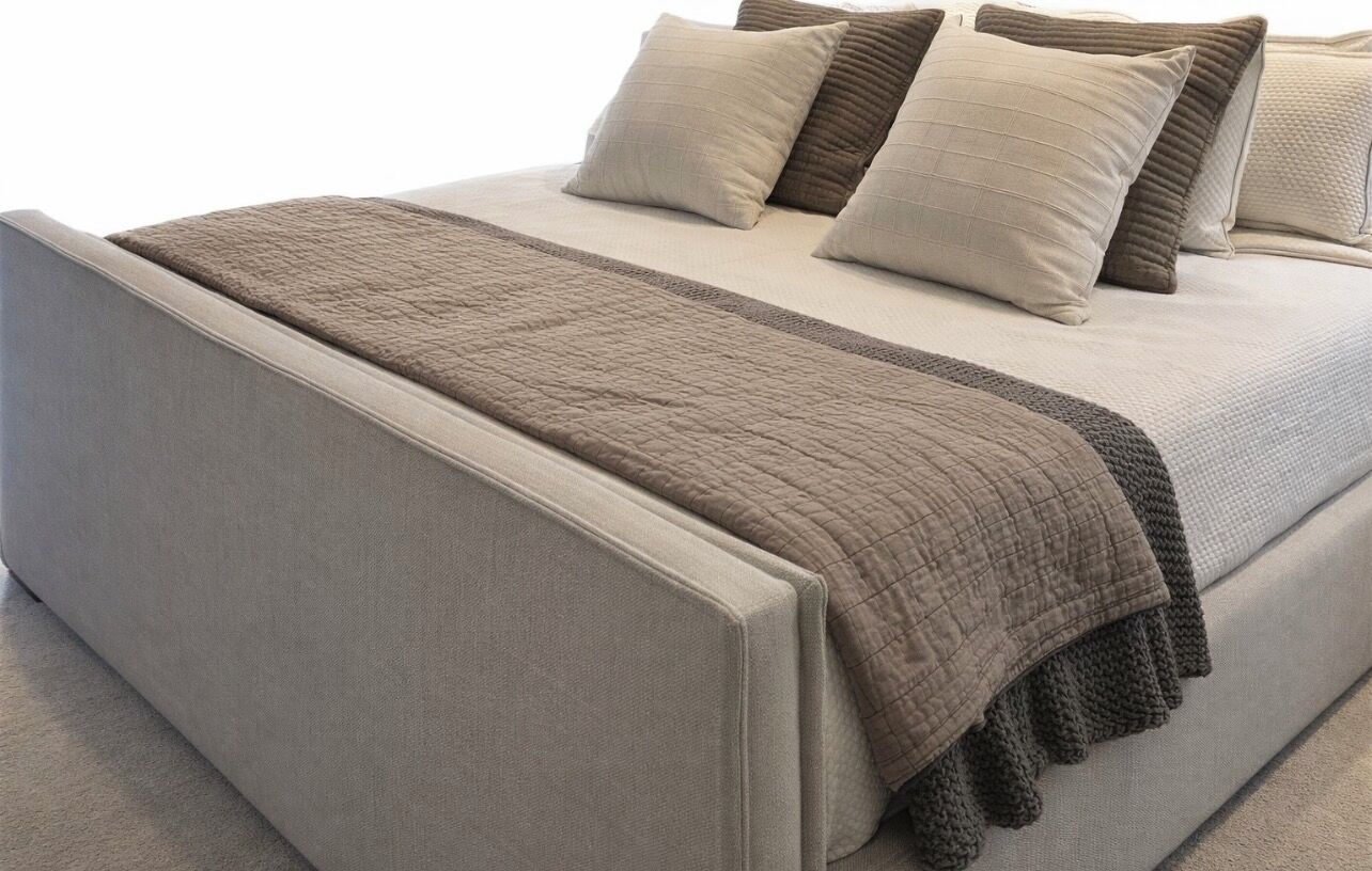 Una cama con cabecera acolchada, colcha en tonos neutros y varias almohadas.