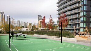 Ein Tennisplatz im Freien mit Netz, umgeben von Bäumen und Gebäuden.